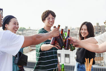 Eine Gruppe junger japanischer Männer und Frauen steht auf einem Dach in einer städtischen Umgebung und trinkt Bier. - MINF14235