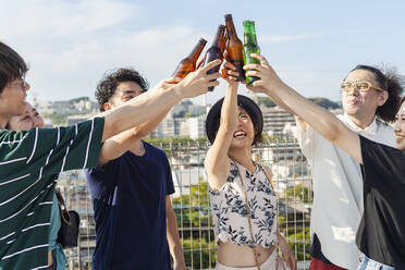 Eine Gruppe junger japanischer Männer und Frauen steht auf einem Dach in einer städtischen Umgebung und trinkt Bier. - MINF14237