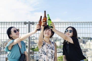 Drei junge Japanerinnen sitzen auf einer Dachterrasse in einer städtischen Umgebung und trinken Bier. - MINF14238