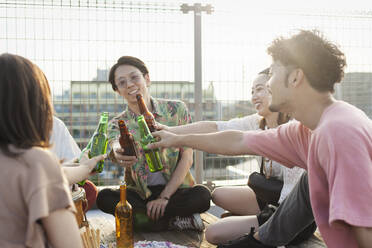 Eine Gruppe junger Japanerinnen und Japaner sitzt auf einer Dachterrasse in einer städtischen Umgebung und trinkt Bier. - MINF14247