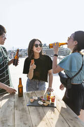 Young Japanese man and two women standing on a rooftop in an urban setting, drinking beer. - MINF14261