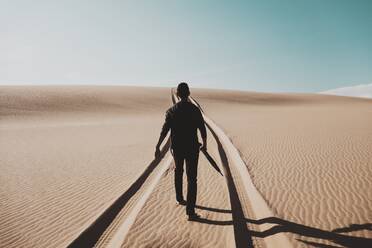 Rear View Of Man Walking On Desert Against Sky - EYF00013