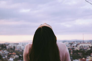 Rear View Of Woman Looking Up With Cityscape In Background Against Cloudy Sky - EYF00034