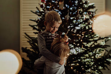 Geschwister stehen gegen den Weihnachtsbaum zu Hause - EYF00087
