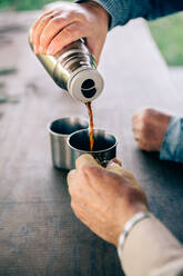 Cropped Hand gießt schwarzen Kaffee in Tasse gehalten von Freund - EYF00098