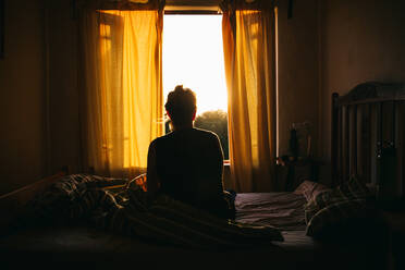 Rear View Of Woman Sitting On Bed At Home - EYF00159