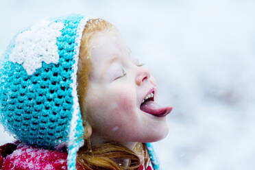 Close-Up Of Girl In Warm Clothing Sticking Out Tongue Outdoors During Snowfall - EYF00306