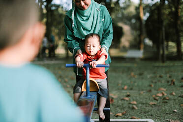 Mother Holding Son Sitting On Seesaw At Playground - EYF00319