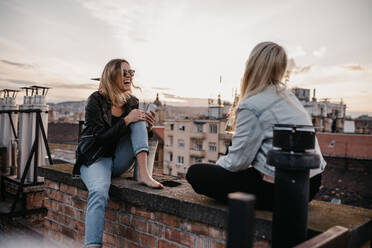 Fröhliche Frauen im Gespräch, während sie auf der Terrasse eines Gebäudes gegen den Himmel sitzen - EYF00345