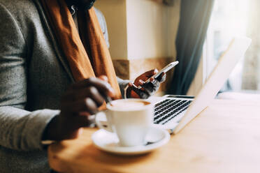 Midsection of Man Using Mobile Phone While Having Coffee In Cafe - EYF00495