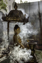 Eine kleine Buddha-Statue in der Sule-Pagode, umgeben von Rauchwolken mit zwei Kinaree-Statuen im Hintergrund, Yangon (Rangun), Myanmar (Burma), Asien - RHPLF14061