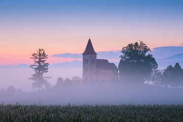 Ländliche gotische Kirche auf einem Friedhof an einem nebligen Morgen. - CAVF77065