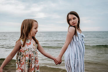 Portrait of sisters holding hands and walking near a lake - CAVF77071