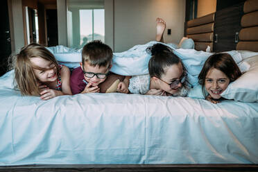Kinder liegen auf dem Bett im Hotelzimmer im Urlaub - CAVF77075