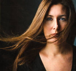 Porträt einer Frau mit langen braunen Haaren, die über ihr Gesicht wehen. - CAVF77089