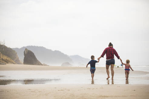 Rückansicht einer Mutter, die mit ihren beiden kleinen Kindern am Strand spazieren geht. - CAVF77121