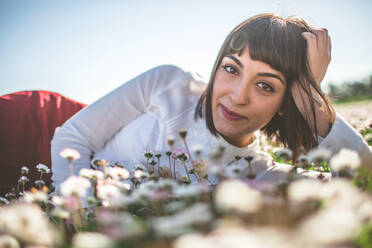 Porträt einer glücklichen jungen Frau, die sich auf einem Blumenfeld entspannt - EYF00651