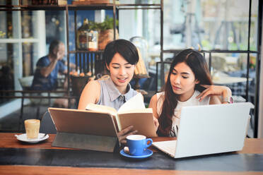 Business Women Reading Book With Laptop And Digital Tablet On Table At Cafe - EYF00687