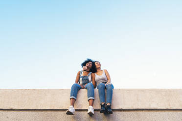 Low Angle View of Female Friends Taking Selfie beim Sitzen auf Stützmauer - EYF00761