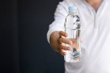 Midsection Of Man Holding Water Bottle While Standing Against Wall stock  photo