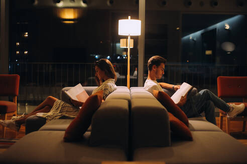 Menschen lesen Bücher, während sie auf dem Sofa im beleuchteten Raum sitzen - EYF00841