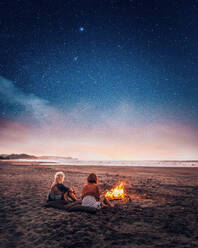 Women Sitting By Bonfire At Beach Against Sky - EYF00967