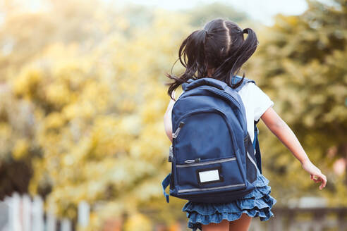 Rückansicht eines Mädchens, das einen Rucksack trägt, während es gegen Bäume läuft - EYF00990