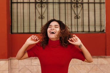 Porträt einer glücklichen Frau mit rotem Kleid, die vor einer roten Wand tanzt - TCEF00234