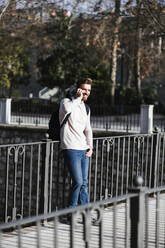 Smiling man on a bridge talking on the phone - LJF01398