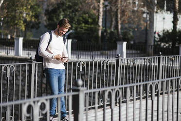 Lächelnder Mann auf einer Brücke mit Mobiltelefon - LJF01399