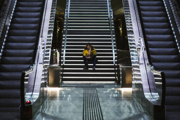 Mann sitzt auf einer Treppe in einer U-Bahn-Station und benutzt ein Mobiltelefon - LJF01405