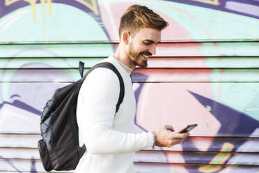 Lächelnder Mann an einer Graffiti-Wand mit Mobiltelefon - LJF01414