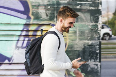 Lächelnder Mann an einer Graffiti-Wand mit Mobiltelefon - LJF01415