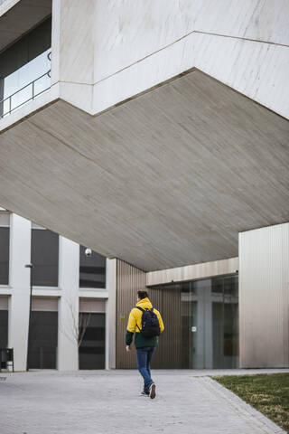 Rückansicht eines Mannes mit Rucksack, der an einem Gebäude in der Stadt entlanggeht, lizenzfreies Stockfoto