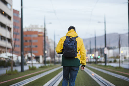 Rückansicht eines Mannes mit Rucksack in der Stadt auf Straßenbahnschienen - LJF01423