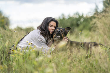 Beautiful young woman embracing dog on plants against sky, Alicante, Alicante Province, Spain - DLTSF00621