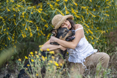 Junge Frau mit Hut, die einen Hund auf Pflanzen umarmt, Alicante, Provinz Alicante, Spanien - DLTSF00624