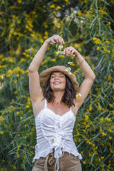 Lächelnde schöne junge Frau, die Blumen auf sich fallen lässt, Alicante, Provinz Alicante, Spanien - DLTSF00629