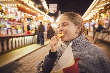 Junges Mädchen isst Kartoffelchips beim nächtlichen Karneval in München, Deutschland - DHEF00149