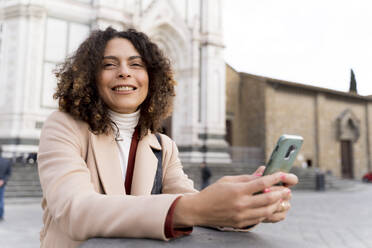 Lächelnde Frau mit Smartphone in der Kirche Santa Croce, Florenz, Italien - FMOF00908