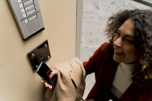 Smiling woman opening door with smartphone - FMOF00912