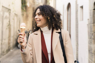 Glückliche Frau isst eine Eiswaffel in einer Gasse, Florenz, Italien - FMOF00923