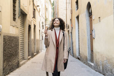 Glückliche Frau isst eine Eiswaffel in einer Gasse, Florenz, Italien - FMOF00924