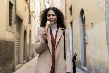 Portrait of smiling woman eating an ice cream cone in an alley, Florence, Italy - FMOF00925