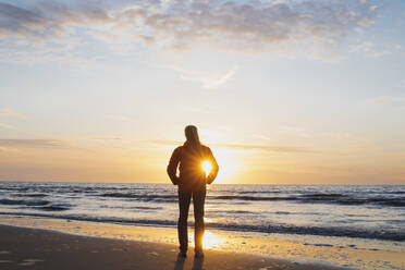 Rückansicht einer Frau in voller Länge, die am Ufer steht und das Meer gegen den Himmel bei Sonnenuntergang betrachtet, Nordseeküste, Flandern, Belgien - GWF06546