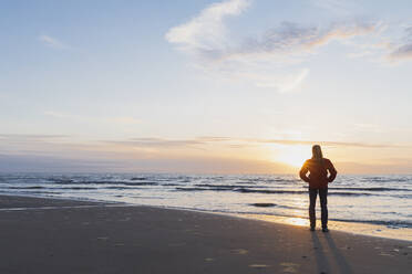 Frau in voller Länge am Ufer stehend mit Blick auf das Meer gegen den Himmel bei Sonnenuntergang, Nordseeküste, Flandern, Belgien - GWF06547