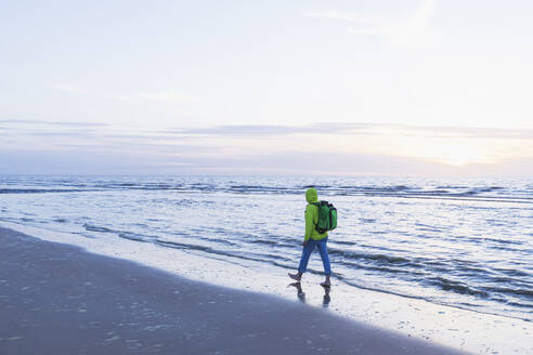 Rentner in voller Länge mit Rucksack, der bei Sonnenuntergang am Strand spazieren geht, Nordseeküste, Flandern, Belgien - GWF06549