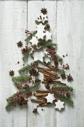 Star shaped cookies, cinnamon sticks, fir twigs, star anise, cookie cutters, pine cones and rose hips arranged into shape of Christmas tree - ASF06602