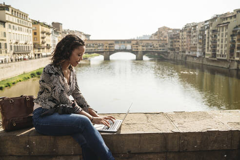 Junge Frau mit Laptop auf einer Brücke, Florenz, Italien - JPIF00447