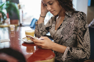 Nahaufnahme einer jungen Frau, die in einem Café ihr Smartphone benutzt - JPIF00449